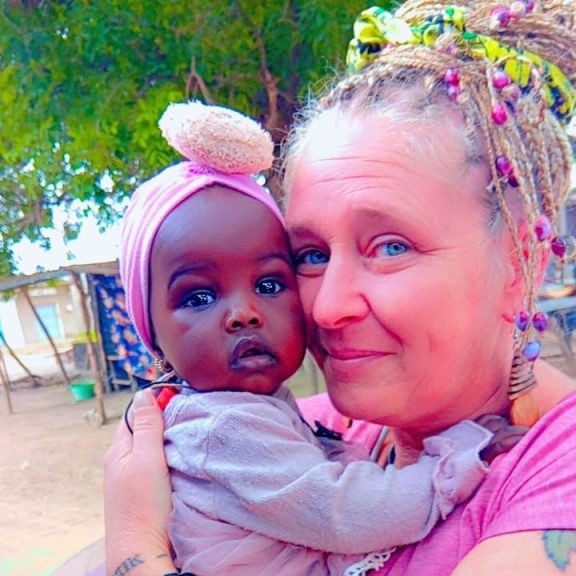 Portrait rapproché d'Emilie, présidente de Racine Partagée, tenant tendrement un enfant sénégalais dans ses bras, illustrant le lien humain et affectif qui unit l'association aux familles locales.